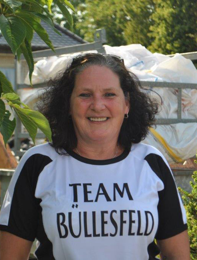 Frau mit schwarzen Haaren lächelt, trägt ein T-Shirt mit der Aufschrift "Team Büllesfeld".