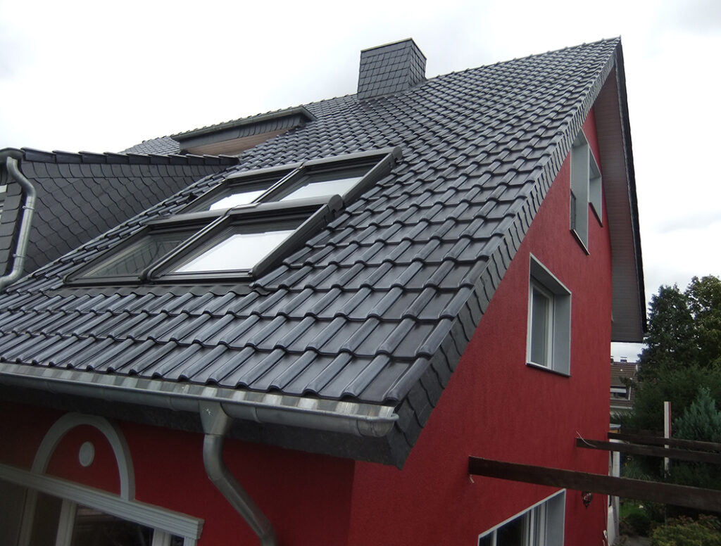 Ein rotes Haus mit schwarzen Dachziegeln und Dachfenstern an einem bewölkten Tag.
