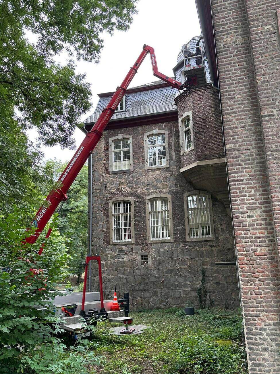 Eine rote Hebebühne erreicht einen Dachbereich an einem alten Backsteingebäude