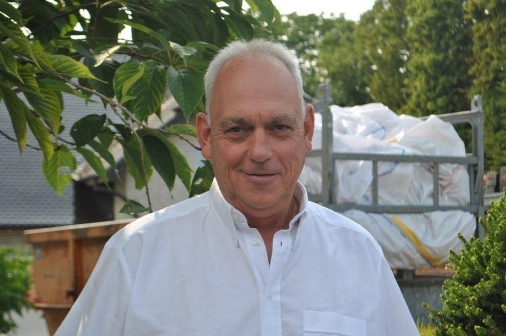 Ein laechelnder aelterer Mann mit grauen Haaren im weissen Hemd im Garten